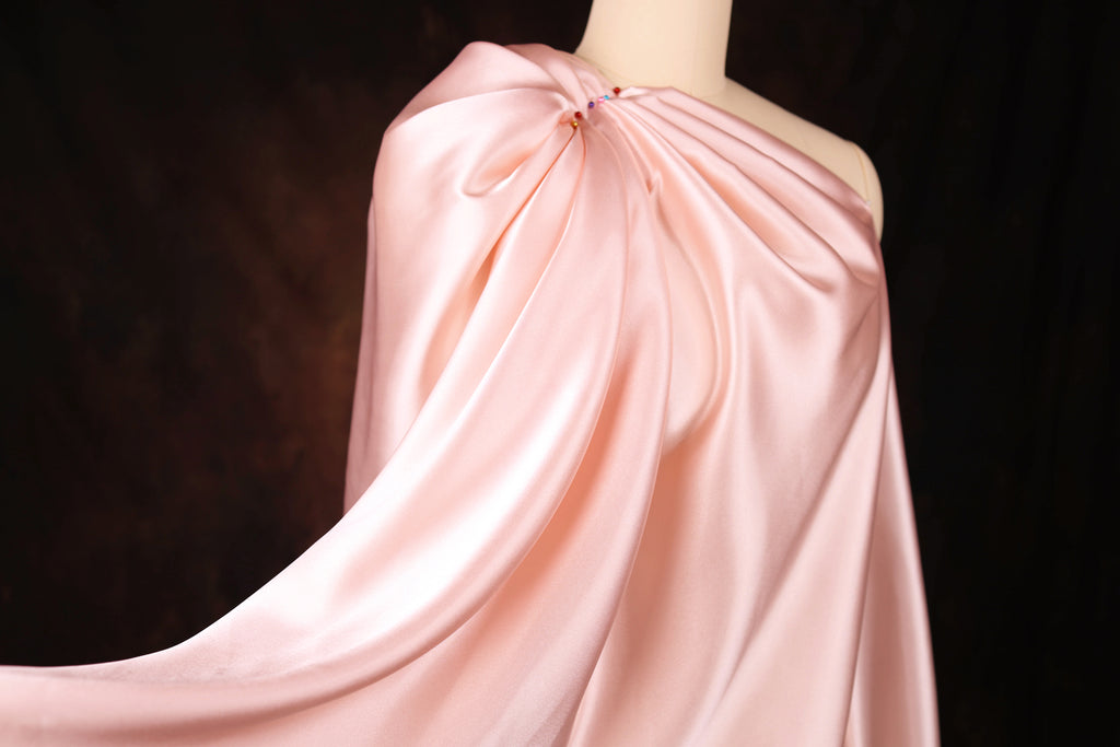 A close-up view of a pink satin fabric draped over a mannequin, with a dark background.