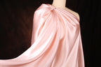 A close-up view of a pink satin fabric draped over a mannequin, with a dark background.