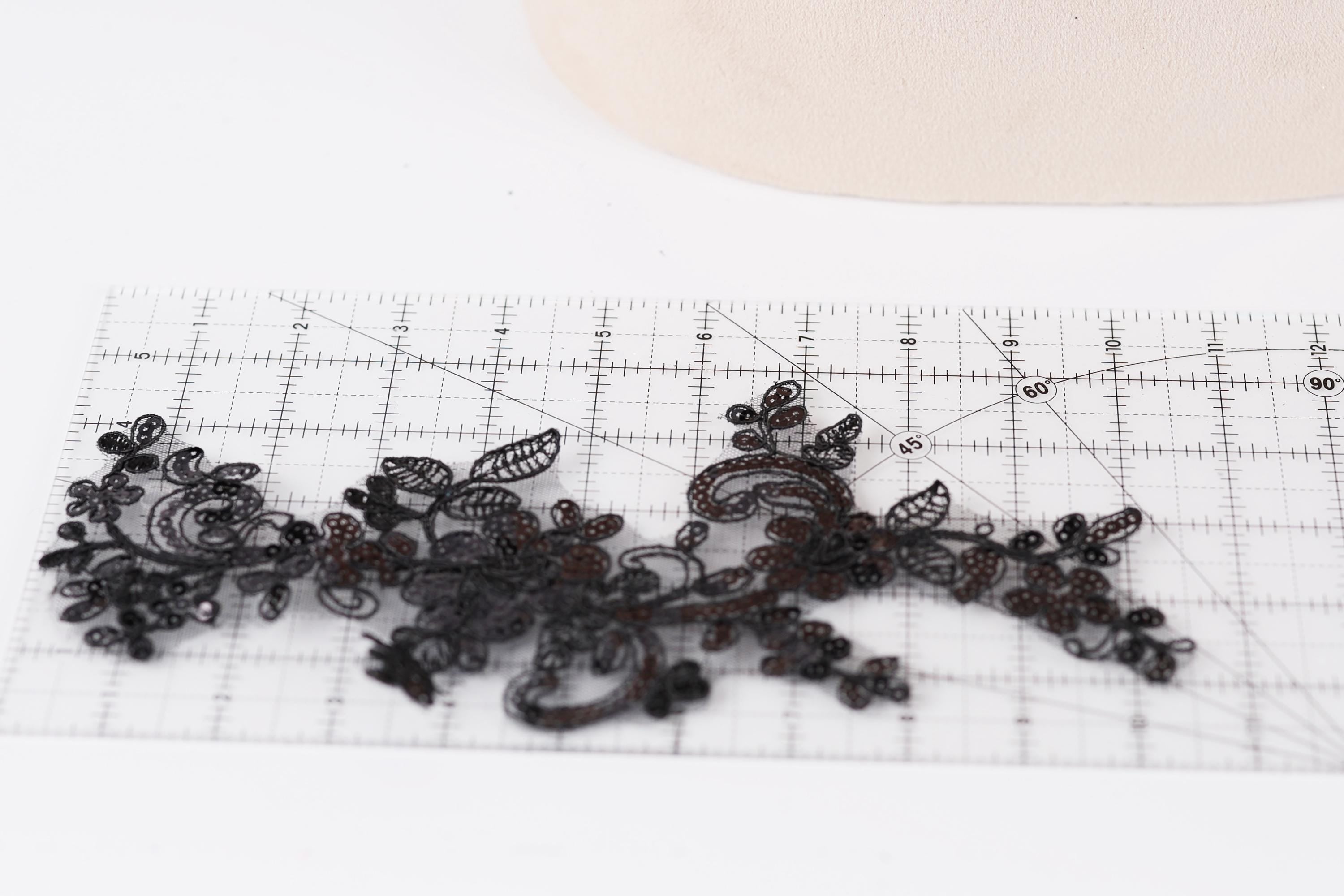 a close-up view of a piece of black lace with intricate floral patterns, placed on a transparent ruler.