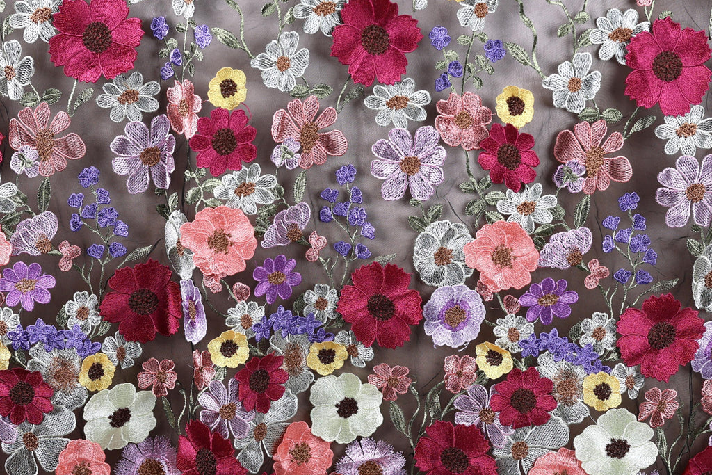 a close-up view of a fabric with a vibrant floral pattern. The fabric is adorned with a variety of colorful flowers, including red, pink, purple, and yellow flowers, as well as green leaves. The flowers are intricately embroidered or stitched onto the fabric, creating a visually striking and detailed design. The image does not contain any text or other discernible objects, and the focus is solely on the floral pattern on the fabric.