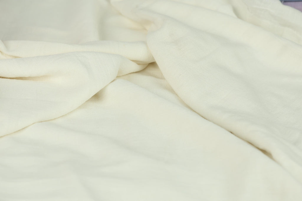 The image is a close-up of a white fabric, possibly a blanket or sheet, with a slightly wrinkled and crumpled appearance.
