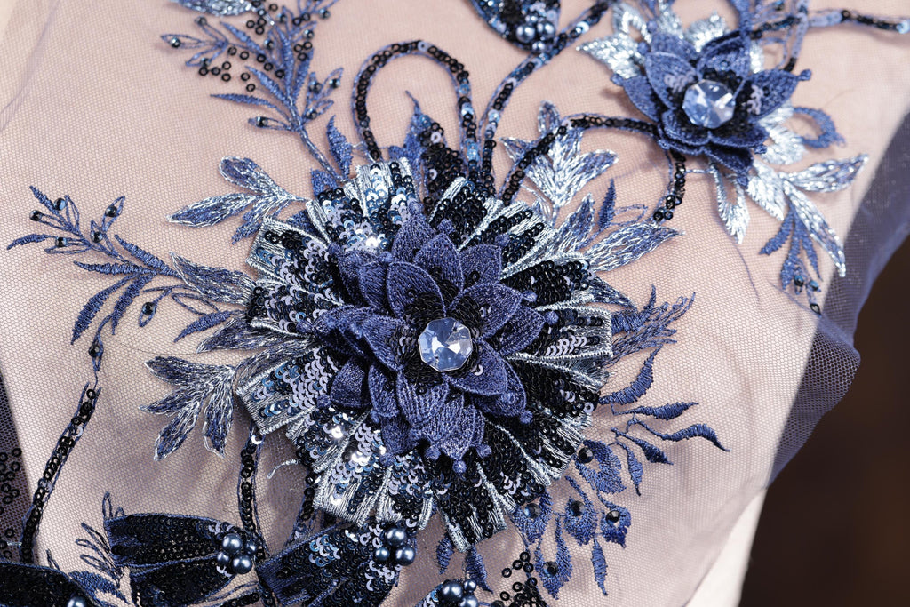 a close-up view of a delicate, intricately designed blue and silver floral embroidery on a fabric.