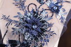 a close-up view of a delicate, intricately designed blue and silver floral embroidery on a fabric.