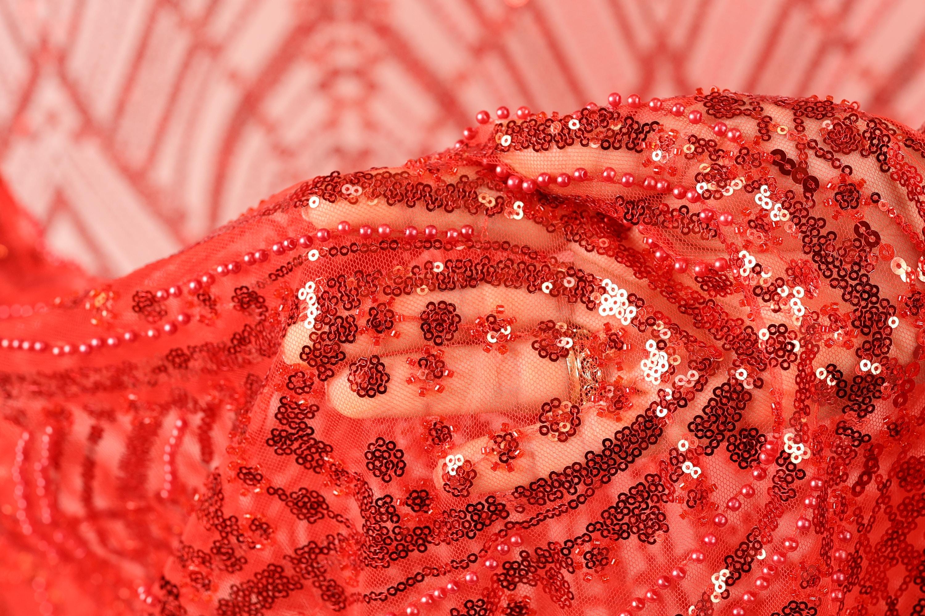 A close-up view of a red sequin fabric, with the intricate patterns and textures of the sequins clearly visible.
