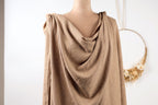 A mannequin wearing a beige draped garment, with a wreath hanging in the background.