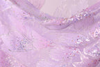 The image is a close-up of a fabric with a purple and pink color scheme, adorned with small, multicolored beads or sequins that create a sparkling, textured effect.