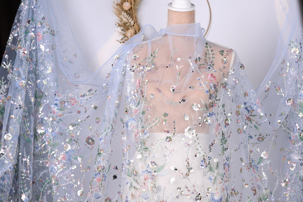 A mannequin wearing a sheer, floral-patterned dress with a sheer, blue-colored fabric draped over it.