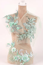 A mannequin wearing a dress with intricate floral embroidery in shades of mint and white.
