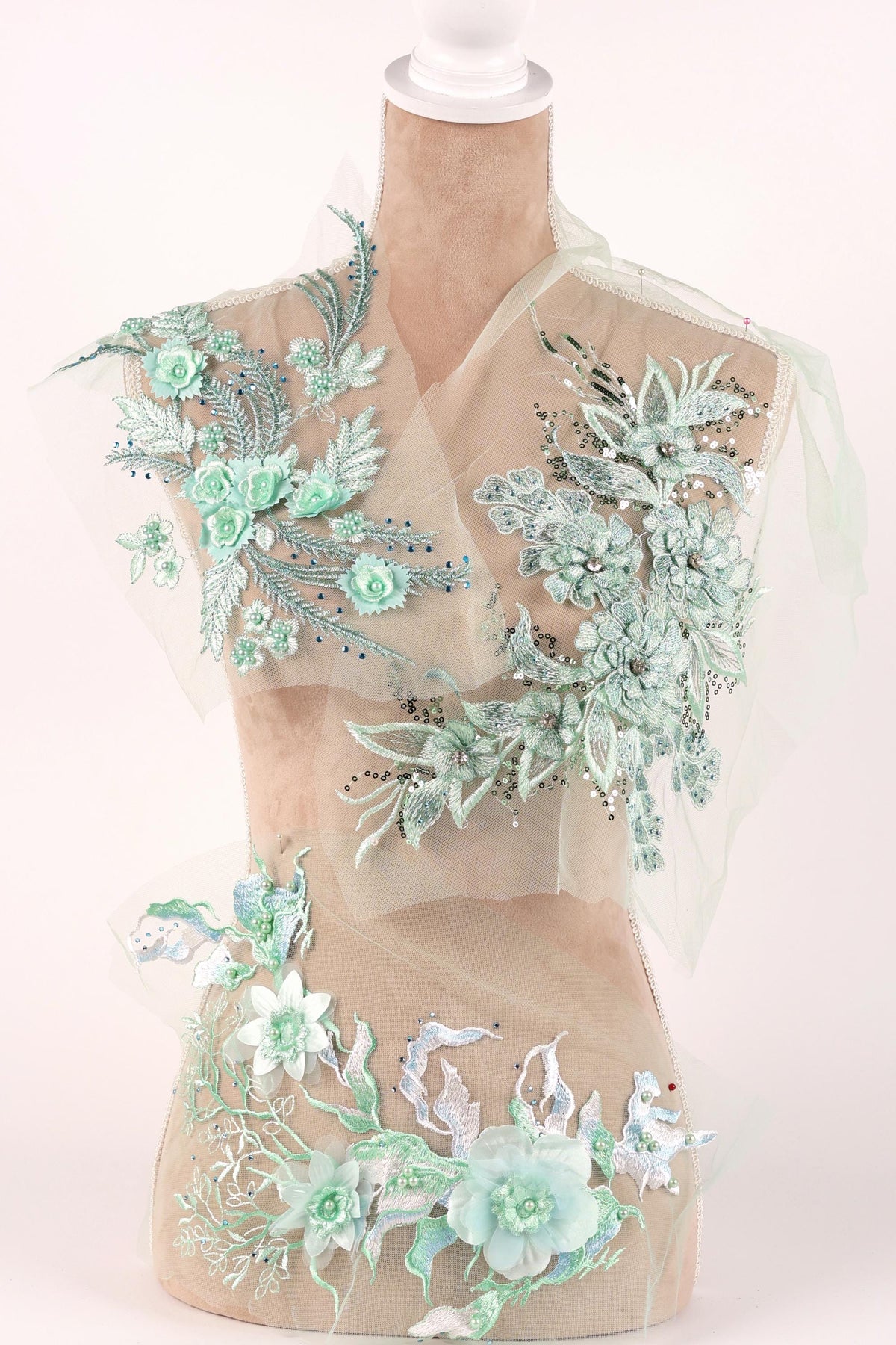 A mannequin wearing a dress with intricate floral embroidery in shades of mint and white.
