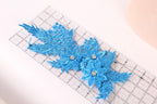a pair of blue glitter flowers with rhinestones, placed on a ruler for size reference.