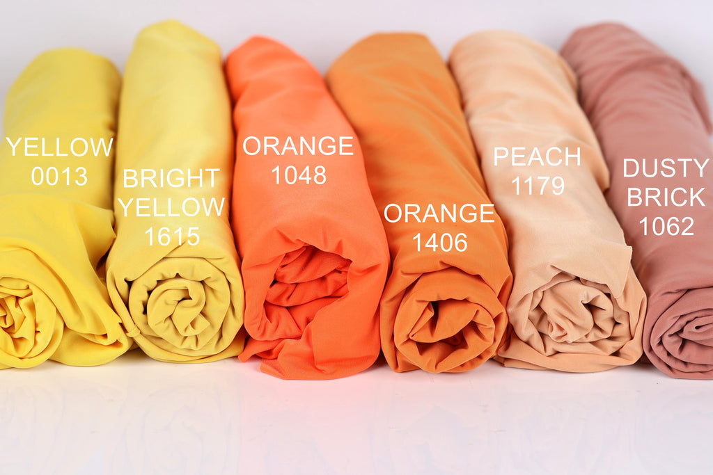a collection of six rolled-up fabric swatches in various colors, including yellow, orange, peach, dusty brick, and peach.