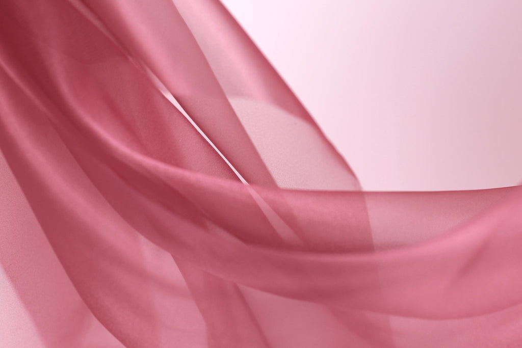 A close-up view of a soft, flowing pink fabric, possibly silk or chiffon, with a delicate, draped appearance.