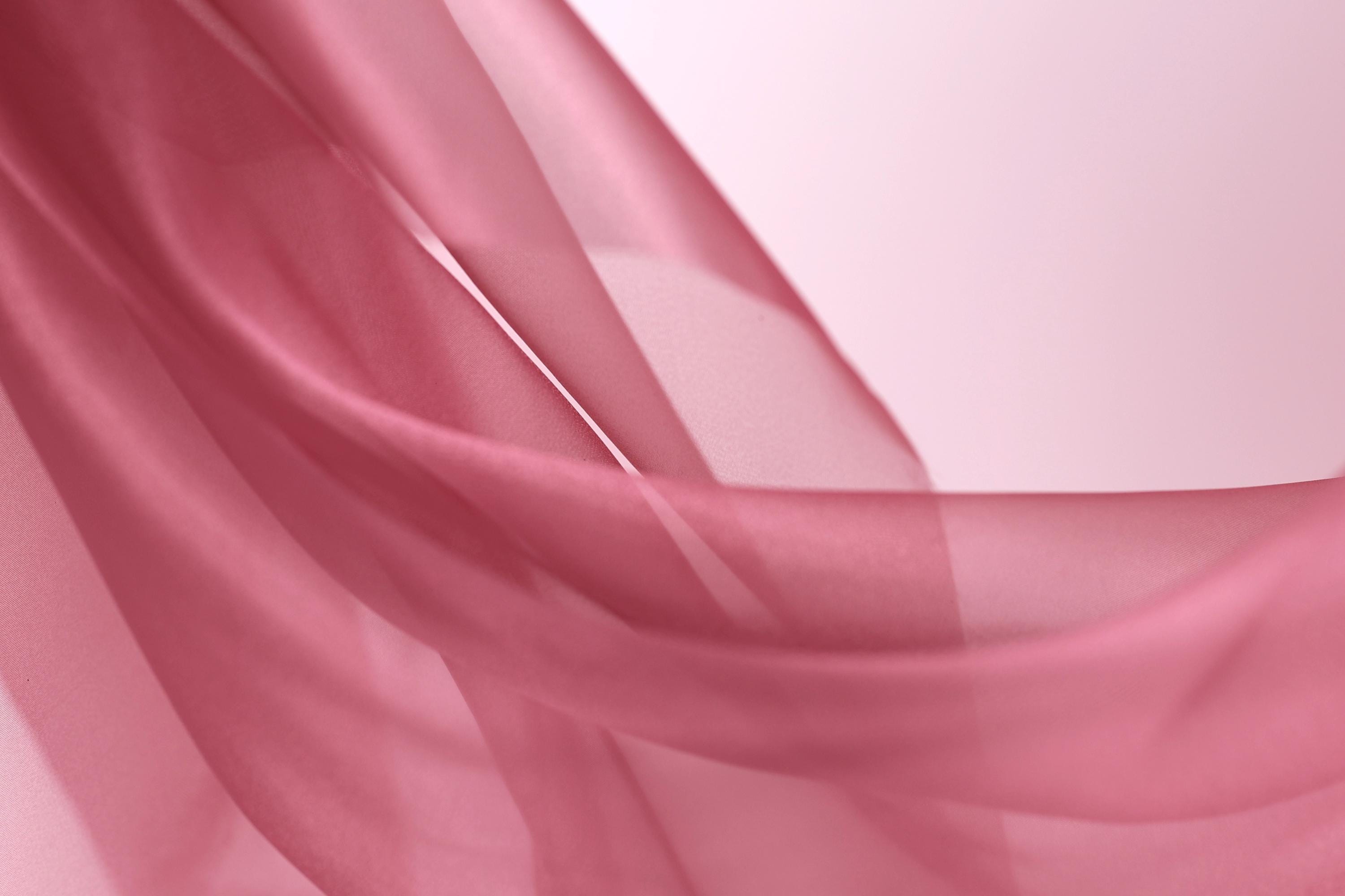 A close-up view of a soft, flowing pink fabric, possibly silk or chiffon, with a delicate, draped appearance.