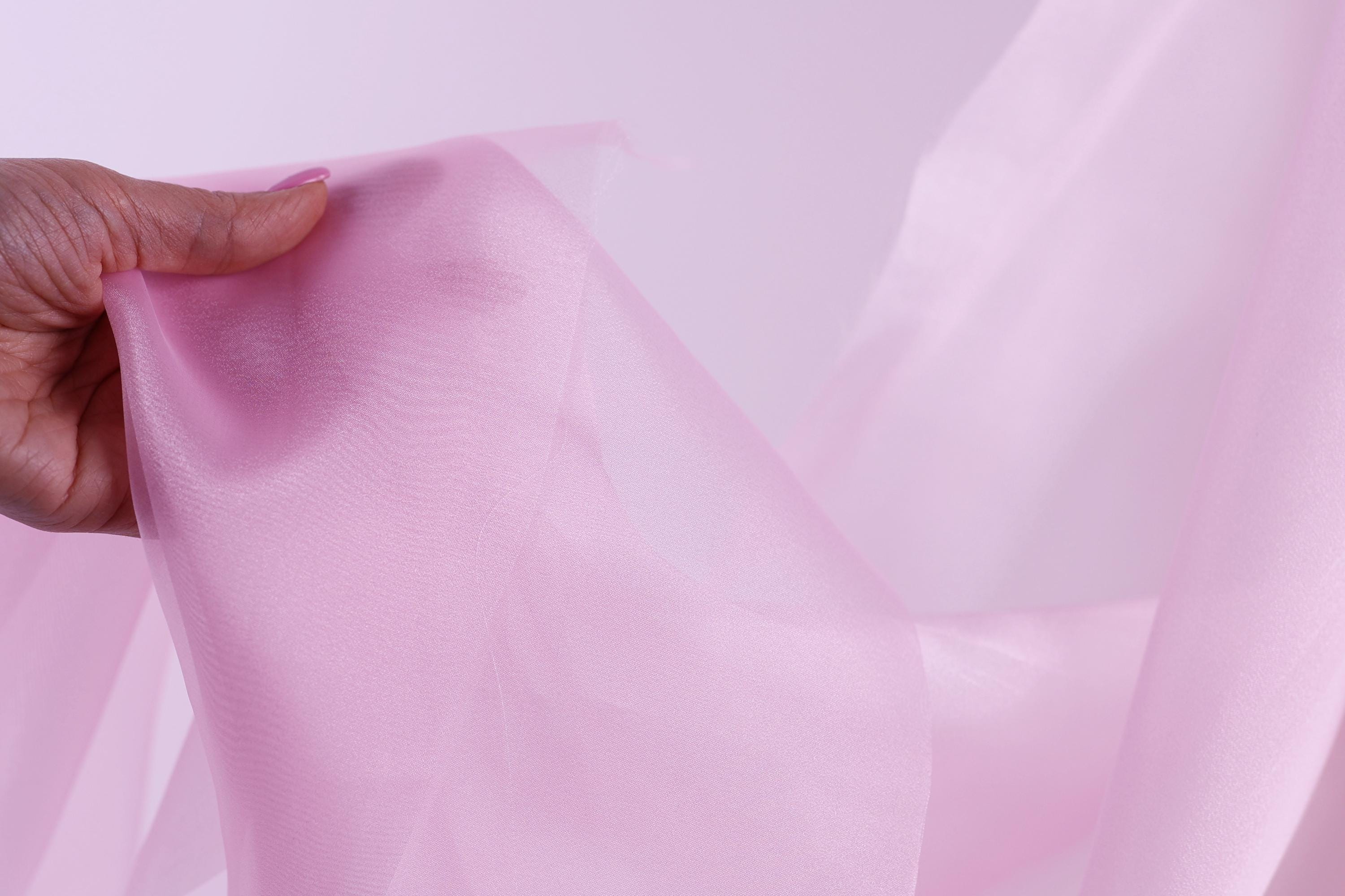 A hand is holding a piece of pink fabric, which appears to be a sheer or sheer-like material.