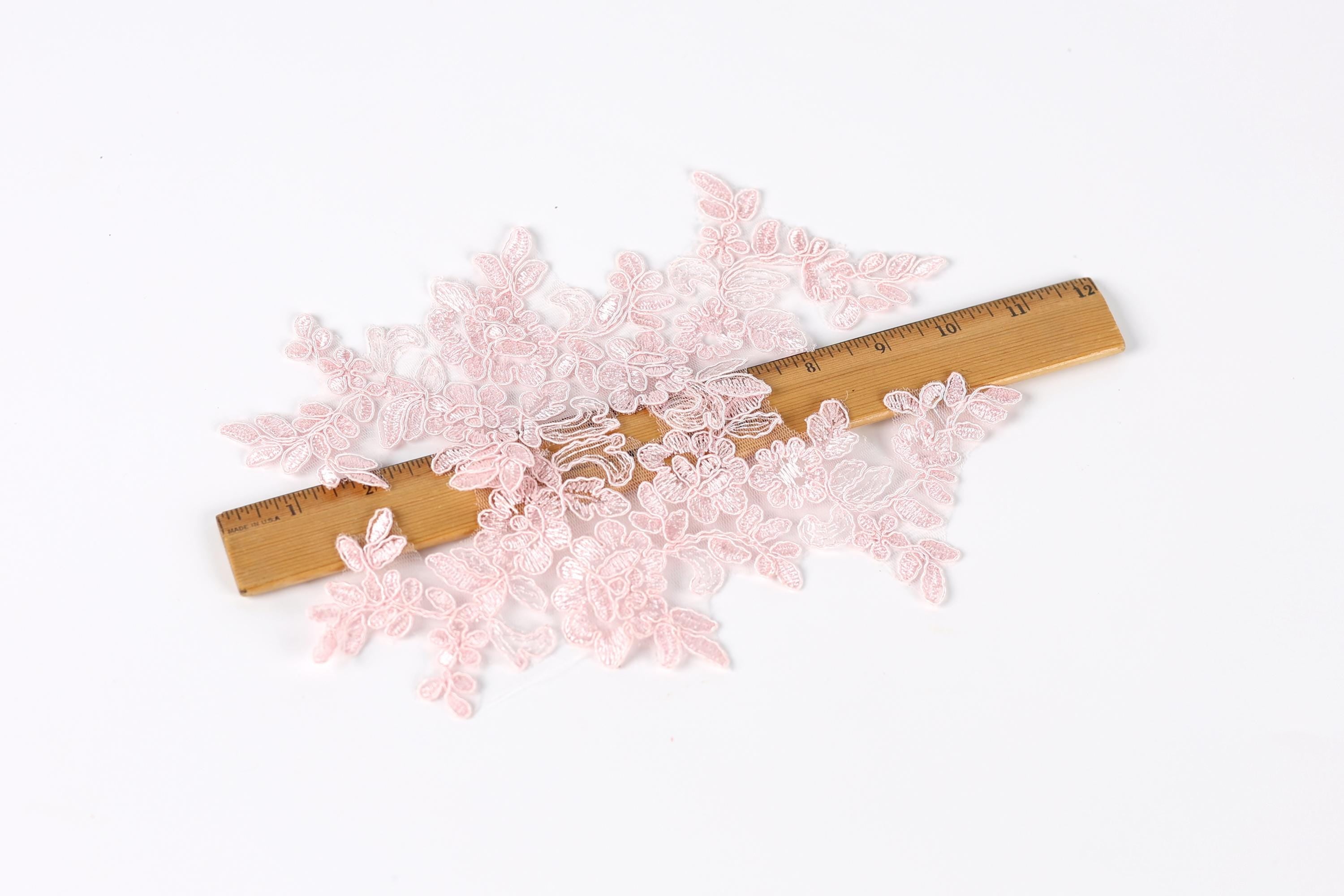 a collection of delicate, pink lace pieces scattered across a wooden ruler, which is placed on a white background.