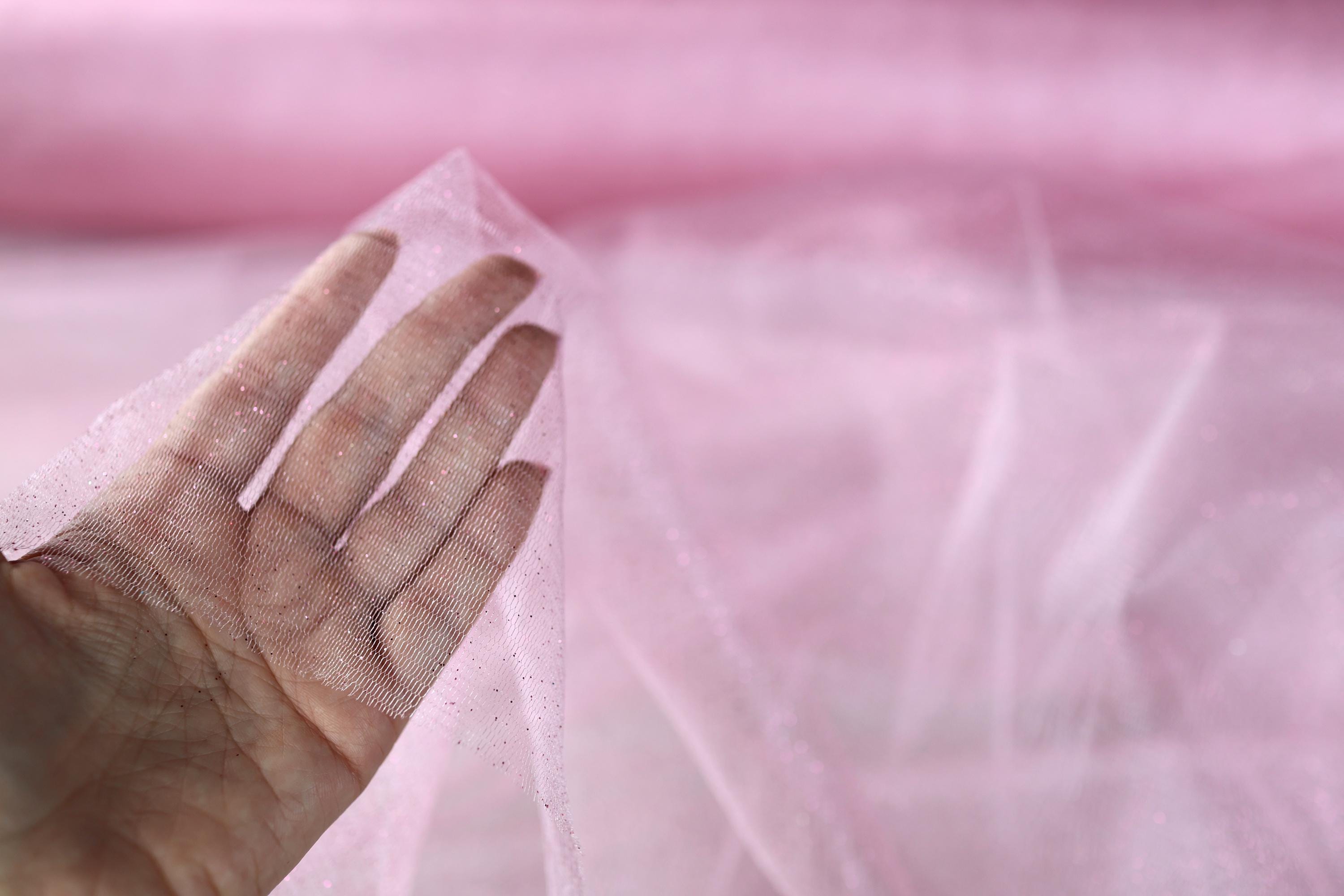 a person's hand holding a piece of pink organine