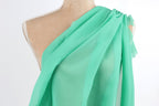 A mannequin wearing a green draped fabric draped over its shoulder.