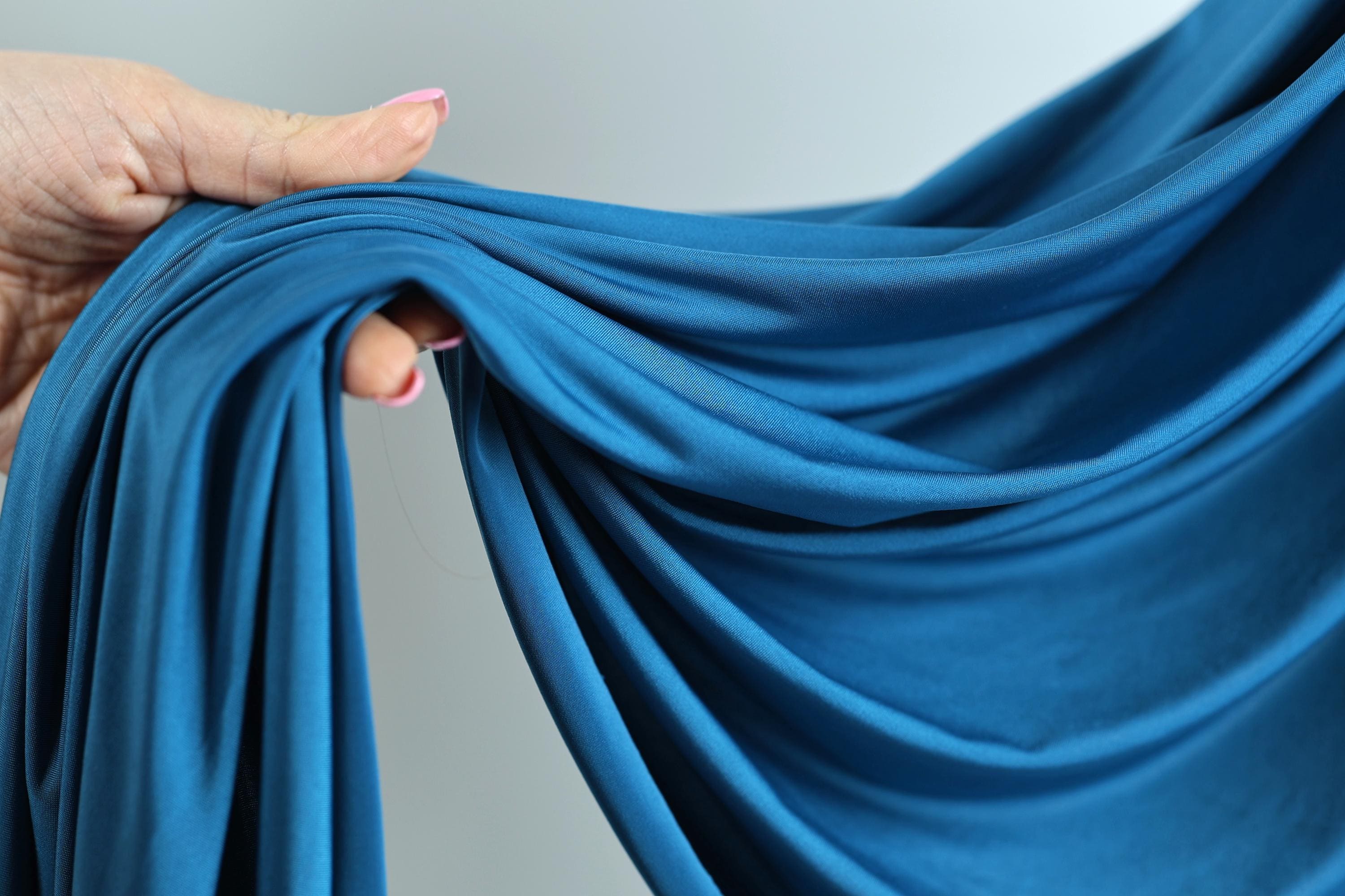 A hand is holding a blue fabric, which appears to be a type of chiffon or sheer material.