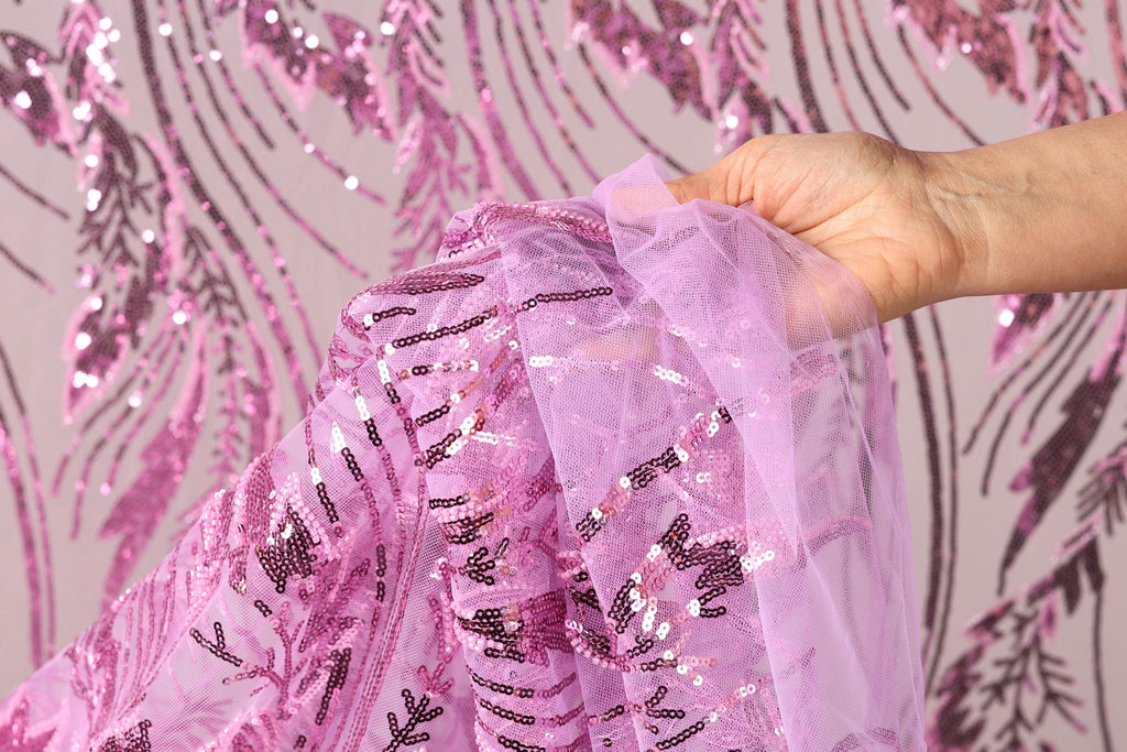 A hand is holding a piece of pink sequin fabric against a background with pink sequin patterns.
