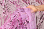 A hand is holding a piece of pink sequin fabric against a background with pink sequin patterns.