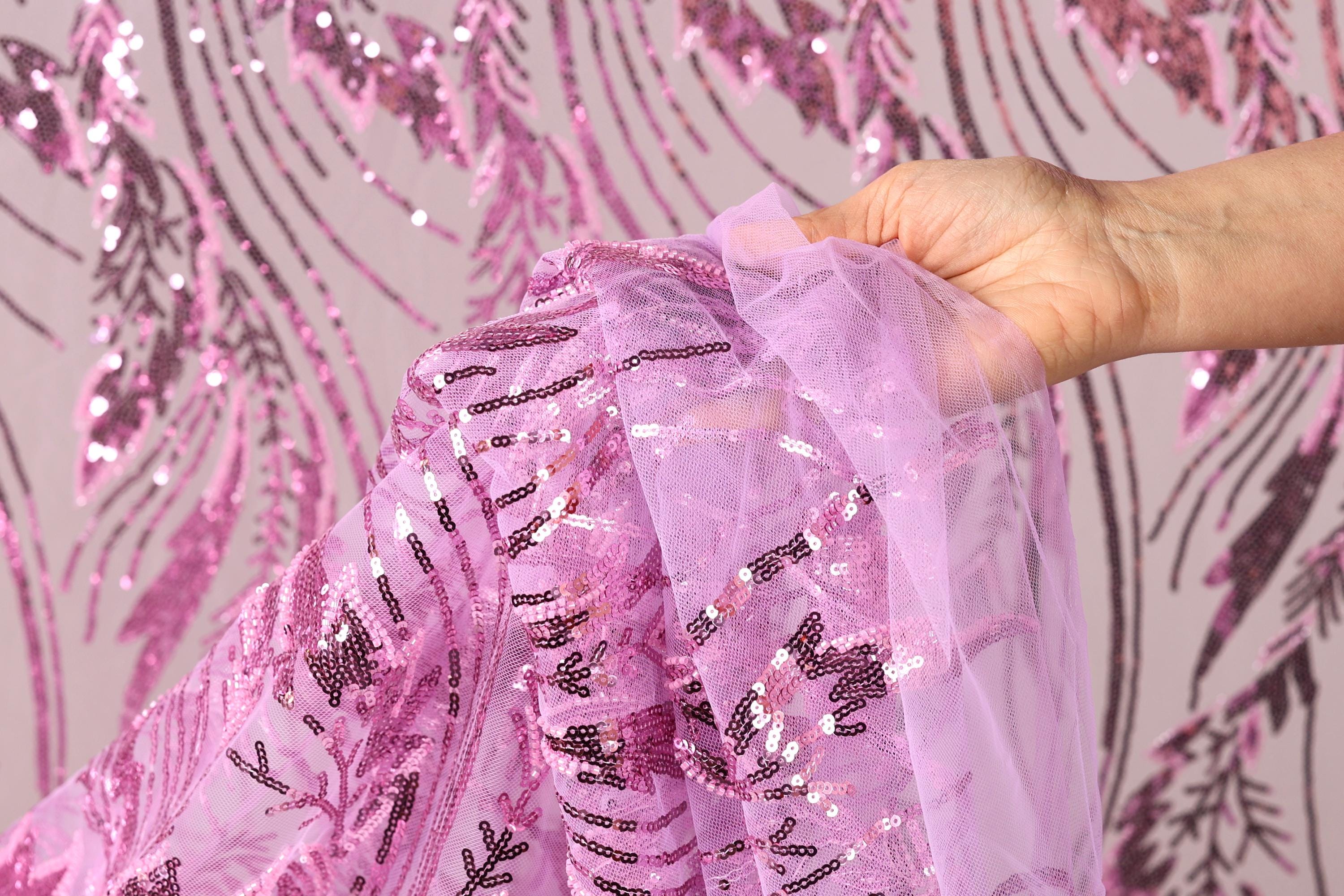 A hand is holding a piece of pink sequin fabric against a background with pink sequin patterns.