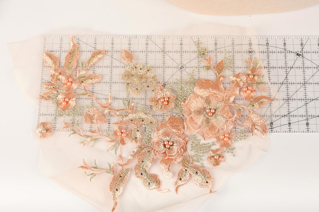 a close-up view of a delicate floral embroidery design, showcasing a variety of peach-colored flowers and leaves. The design is meticulously crafted, with each flower and leaf intricately detailed, creating a visually appealing and harmonious composition.