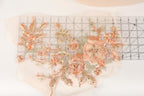 a close-up view of a delicate floral embroidery design, showcasing a variety of peach-colored flowers and leaves. The design is meticulously crafted, with each flower and leaf intricately detailed, creating a visually appealing and harmonious composition.