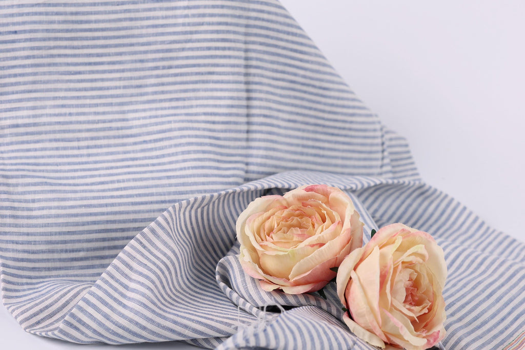 Two pink roses resting on a blue and white striped fabric.