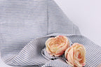 Two pink roses resting on a blue and white striped fabric.