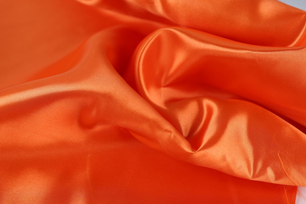 a close-up view of a crumpled orange fabric, with a smooth and shiny surface.