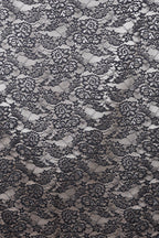 The image is a close-up view of a black and white lace pattern, featuring intricate floral and leaf designs. The lace appears to be a decorative textile, possibly used for clothing or home decor.