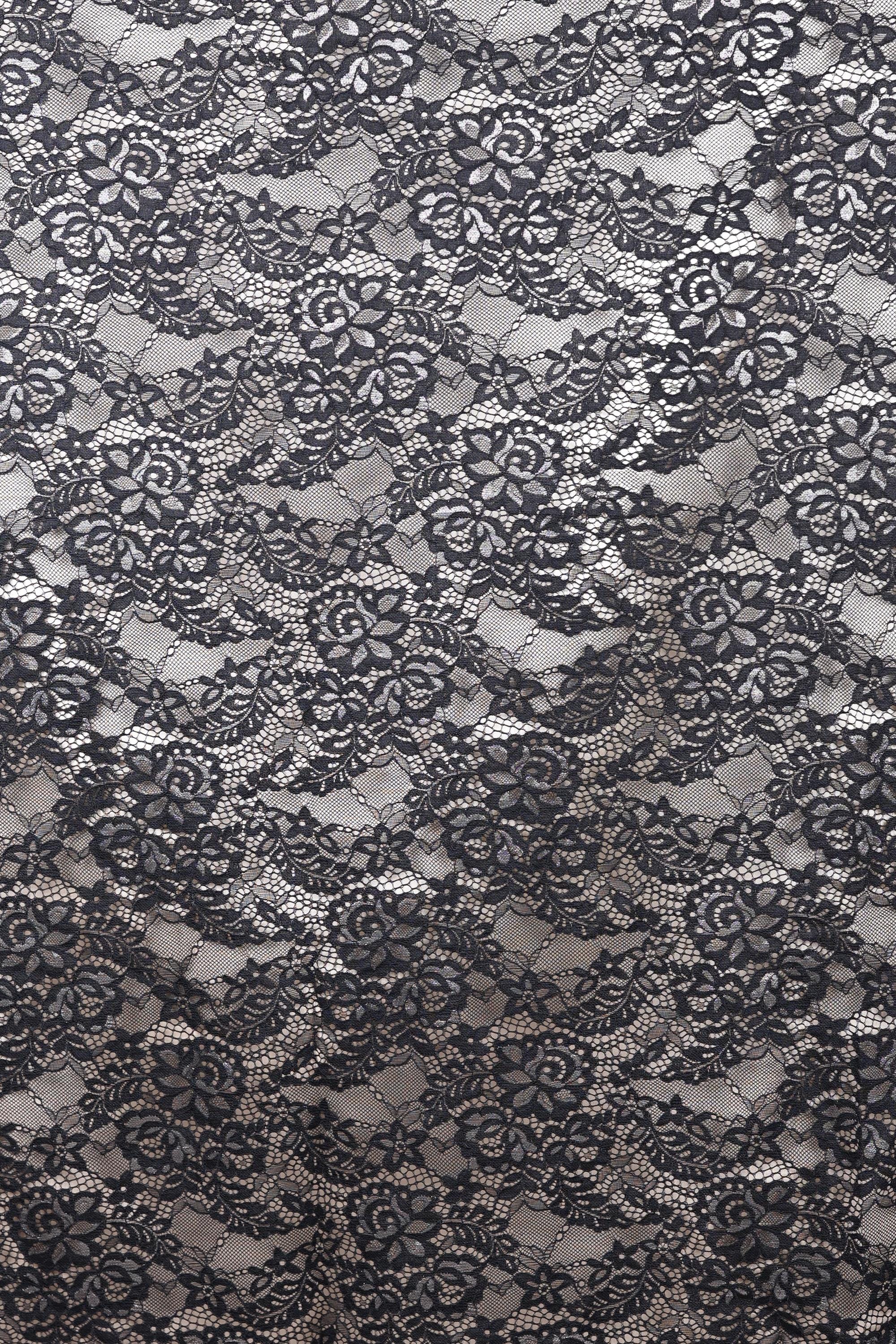The image is a close-up view of a black and white lace pattern, featuring intricate floral and leaf designs. The lace appears to be a decorative textile, possibly used for clothing or home decor.
