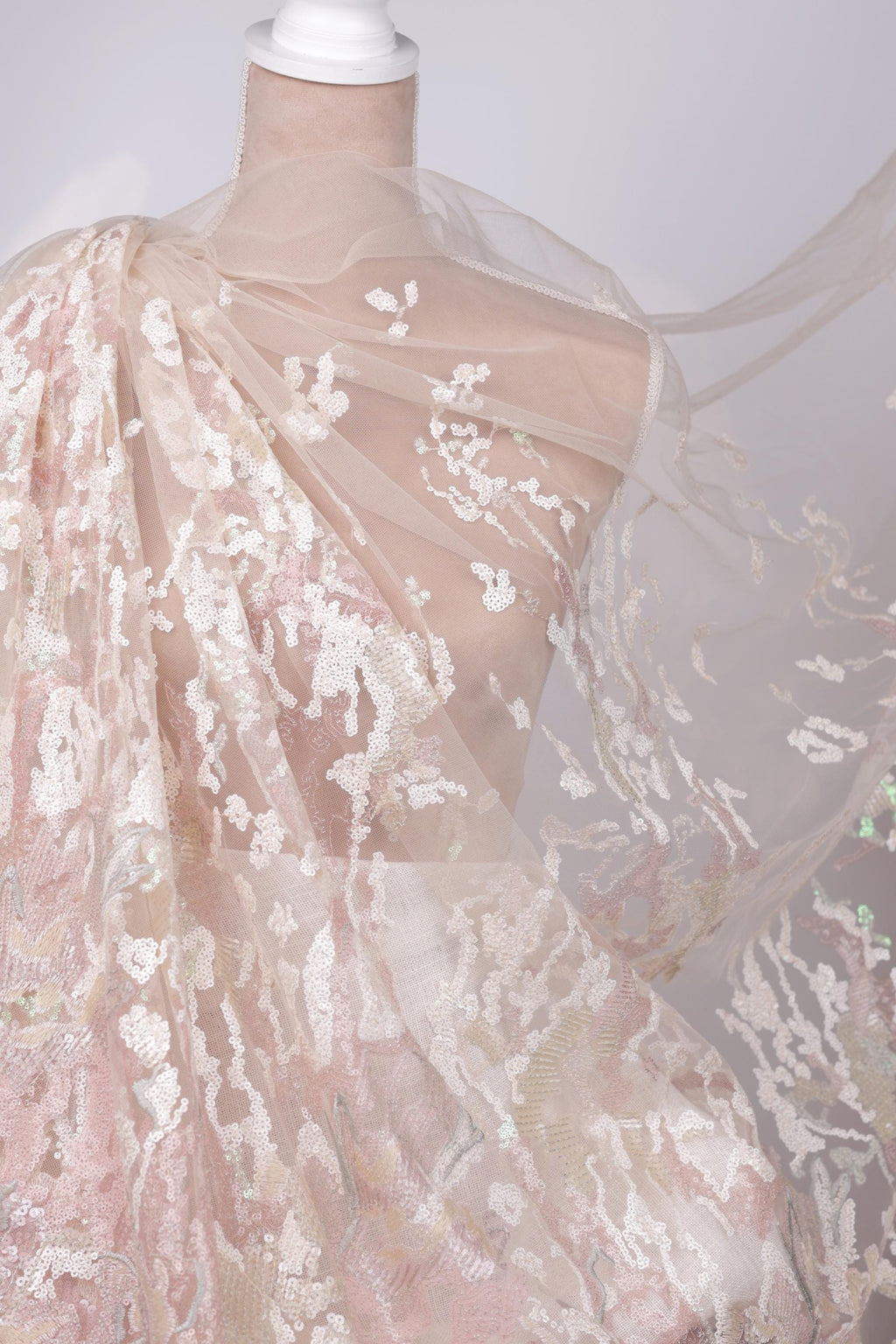 A mannequin wearing a delicate, lace-like dress with a flowing, sheer fabric draped over it.