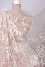 A mannequin wearing a delicate, lace-like dress with a flowing, sheer fabric draped over it.