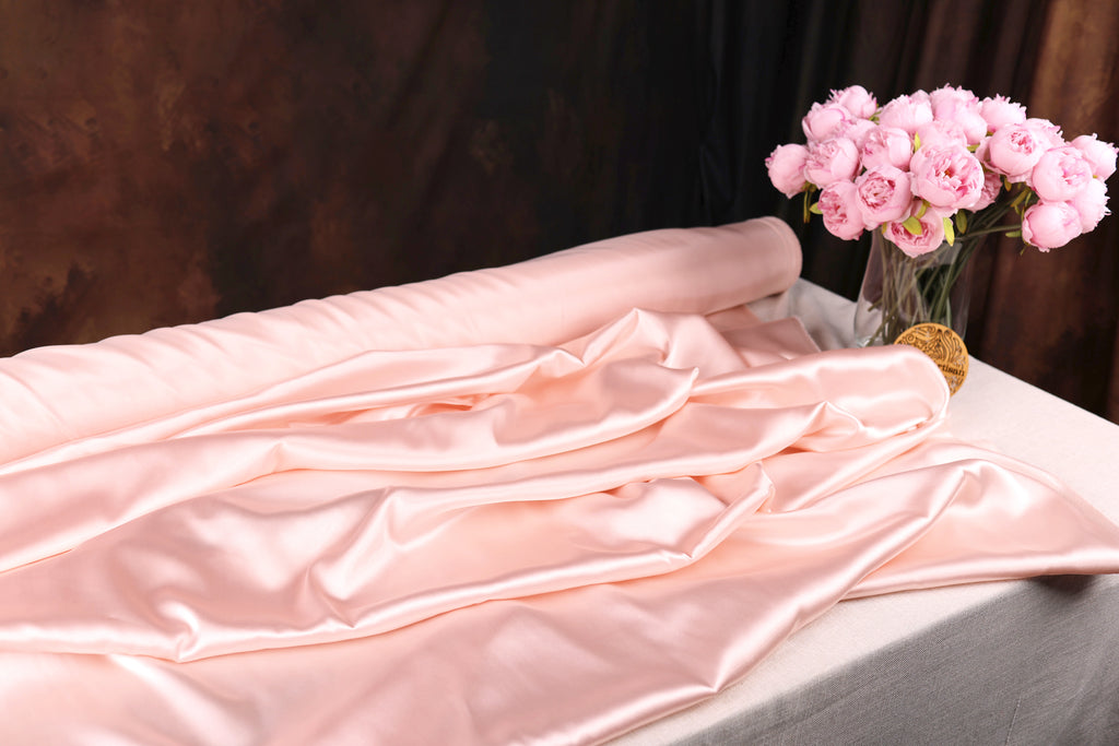 a pink satin fabric draped over a table, with a vase of pink roses placed next to it.
