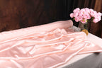 a pink satin fabric draped over a table, with a vase of pink roses placed next to it.