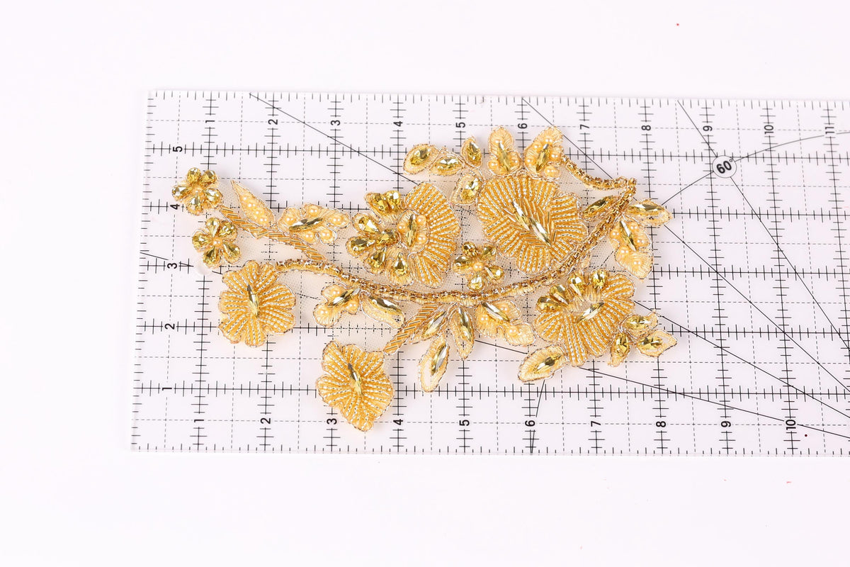a decorative piece with gold-colored flowers and leaves, placed on a ruler for scale.