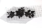 a close-up view of a piece of fabric with black lace or embroidery designs, placed on a transparent ruler or measuring mat.