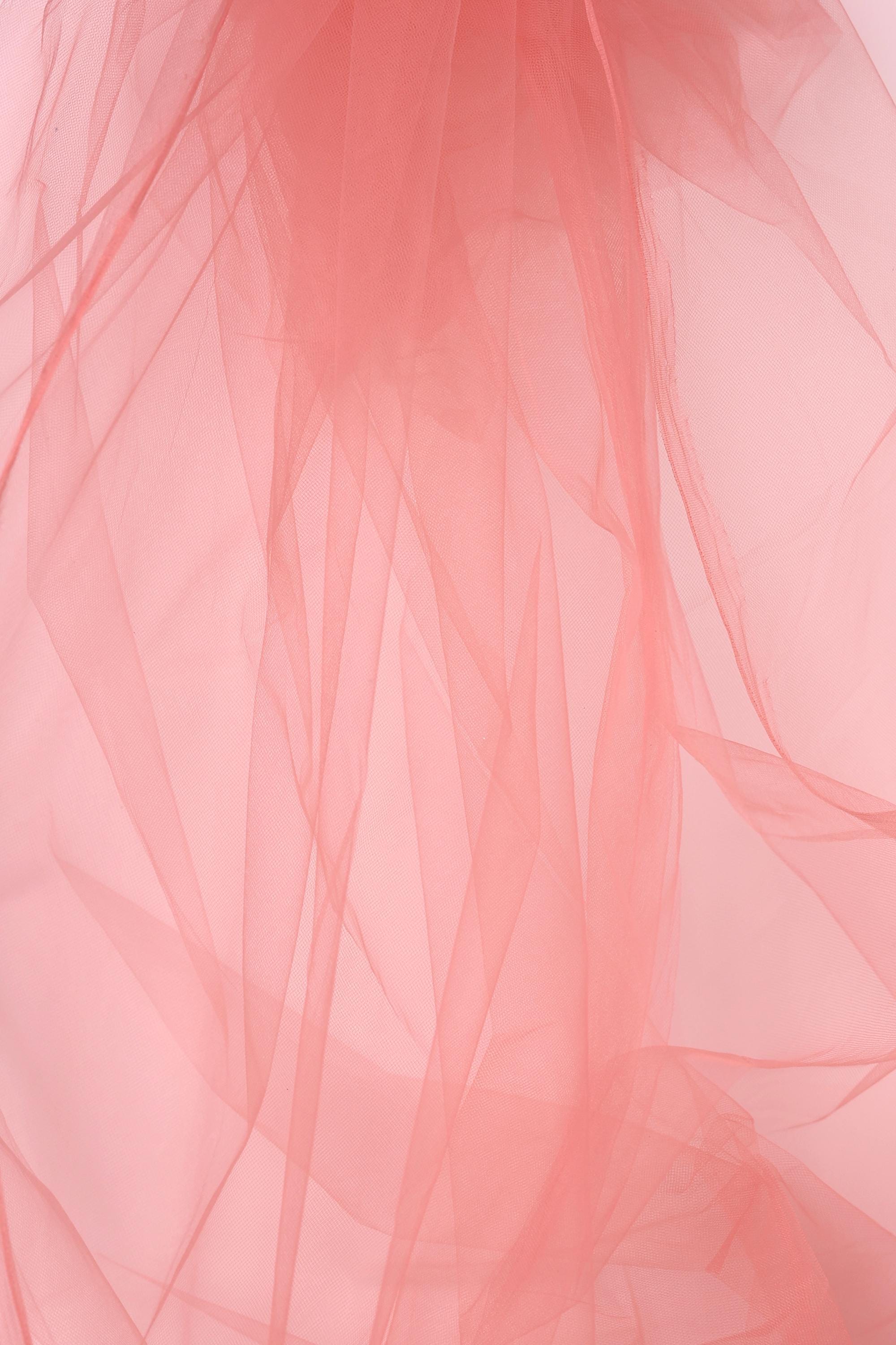 The image is a close-up of a pink, flowing fabric, possibly tulle, with a soft, delicate texture.