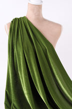 A close-up view of a green velvet fabric draped over a person's leg, with a white heel visible.
