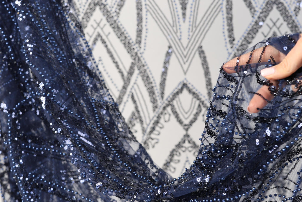 A close-up view of a hand holding a piece of blue sequin fabric, with a patterned background.