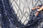 A close-up view of a hand holding a piece of blue sequin fabric, with a patterned background.