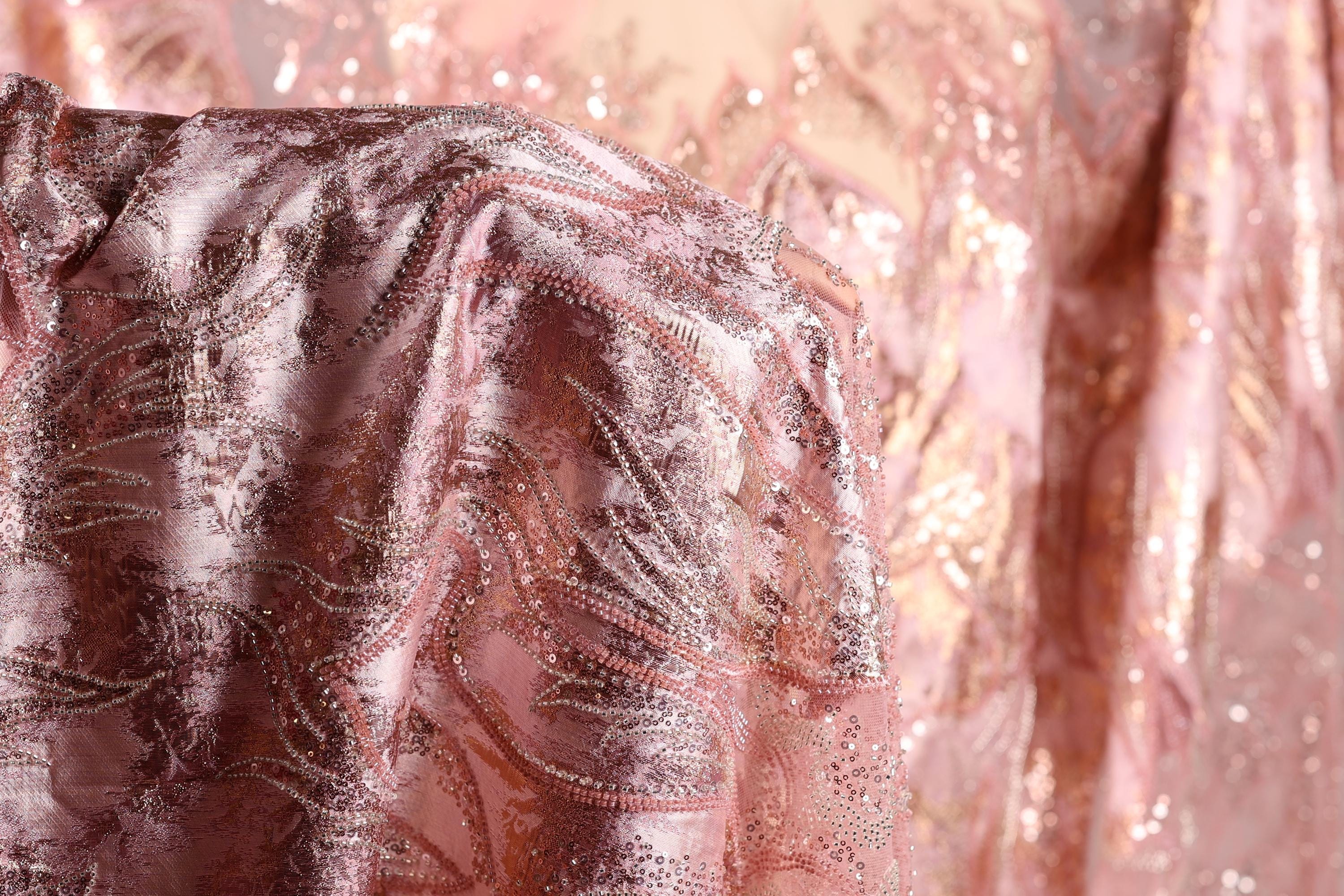 a close-up view of a fabric with a pink and gold sequined pattern, featuring a delicate and intricate design.