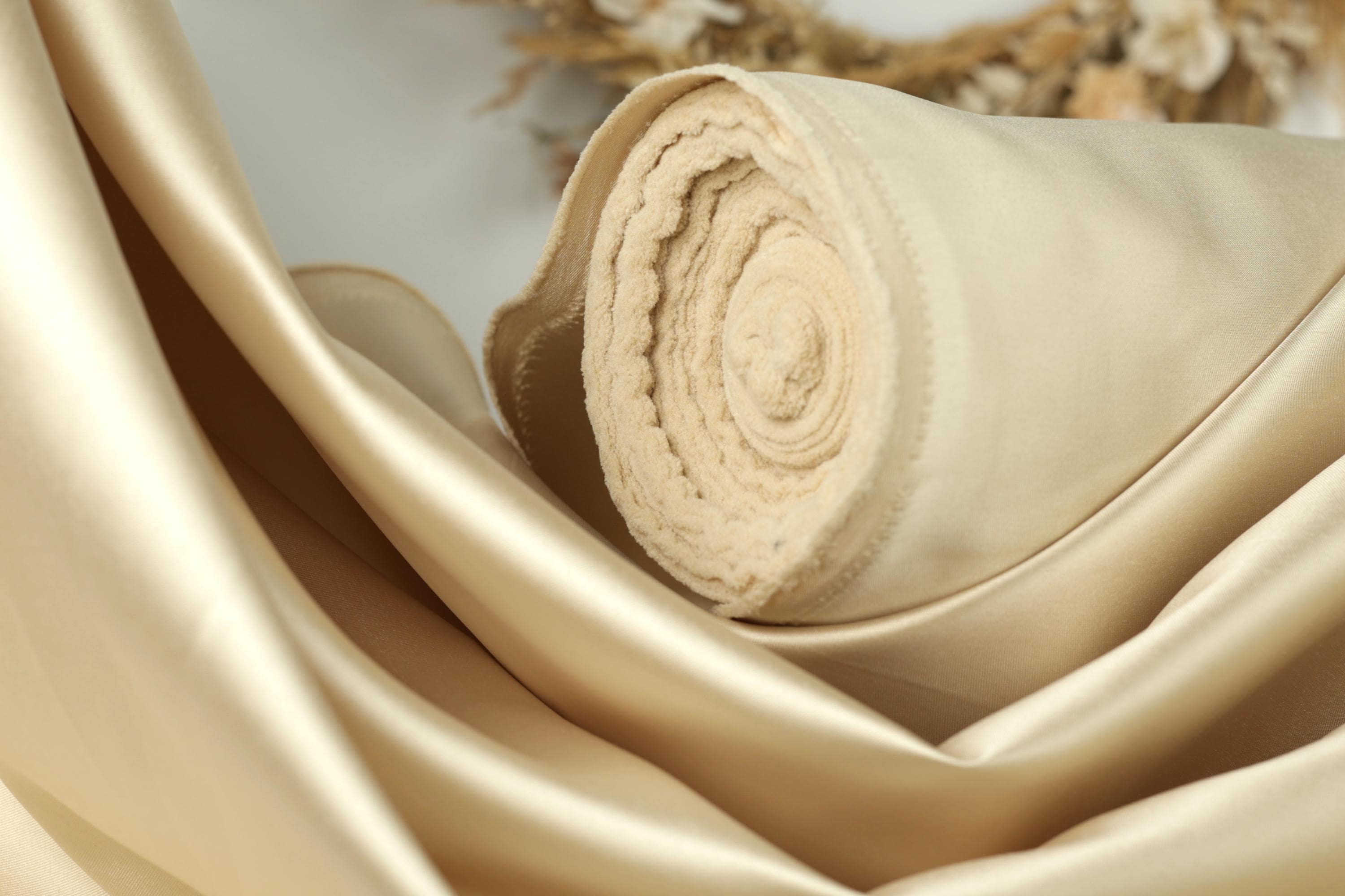 A close-up view of a beige fabric, possibly silk or satin, with a curled edge and a soft, smooth texture.