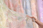 A hand is holding up a piece of fabric with a colorful, patterned design, likely a piece of clothing or textile.