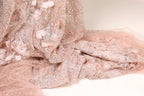 a close-up view of a delicate, pink, and beige fabric with a floral pattern. The fabric appears to be made of lace or sheer material, with a soft and delicate texture.