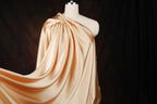 A mannequin wearing a flowing, draped fabric in a light peach color against a dark background.