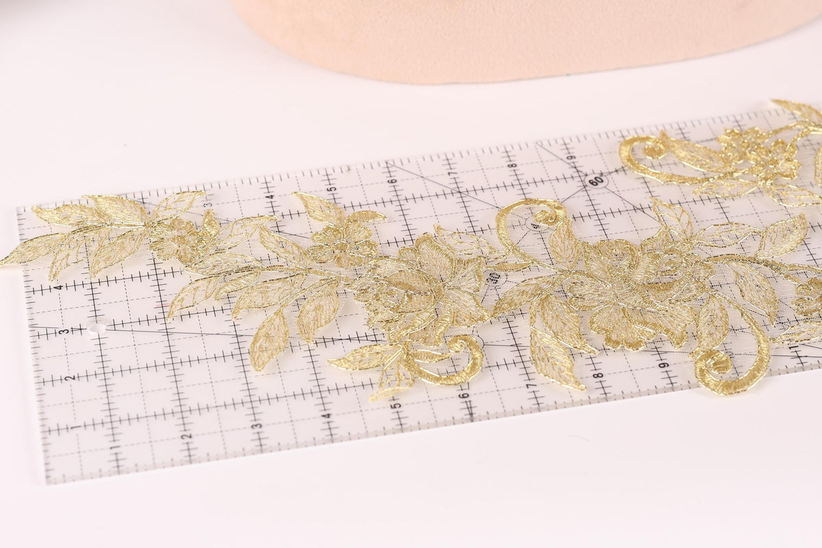 a close-up view of a clear ruler with gold embroidered flowers placed on it.