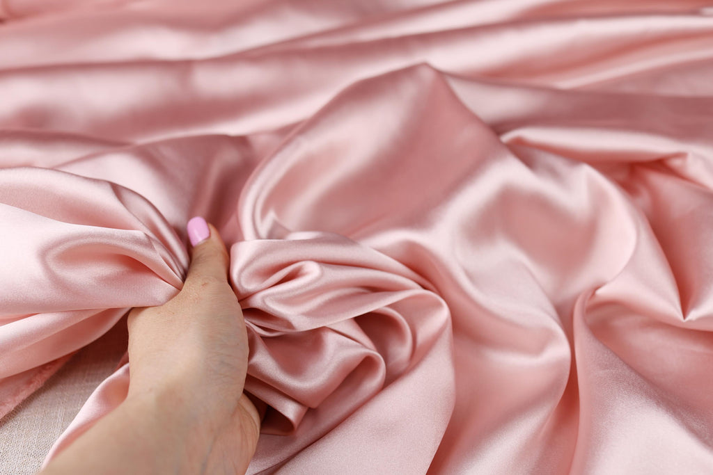 a woman&#39;s hand on a pink satin fabric