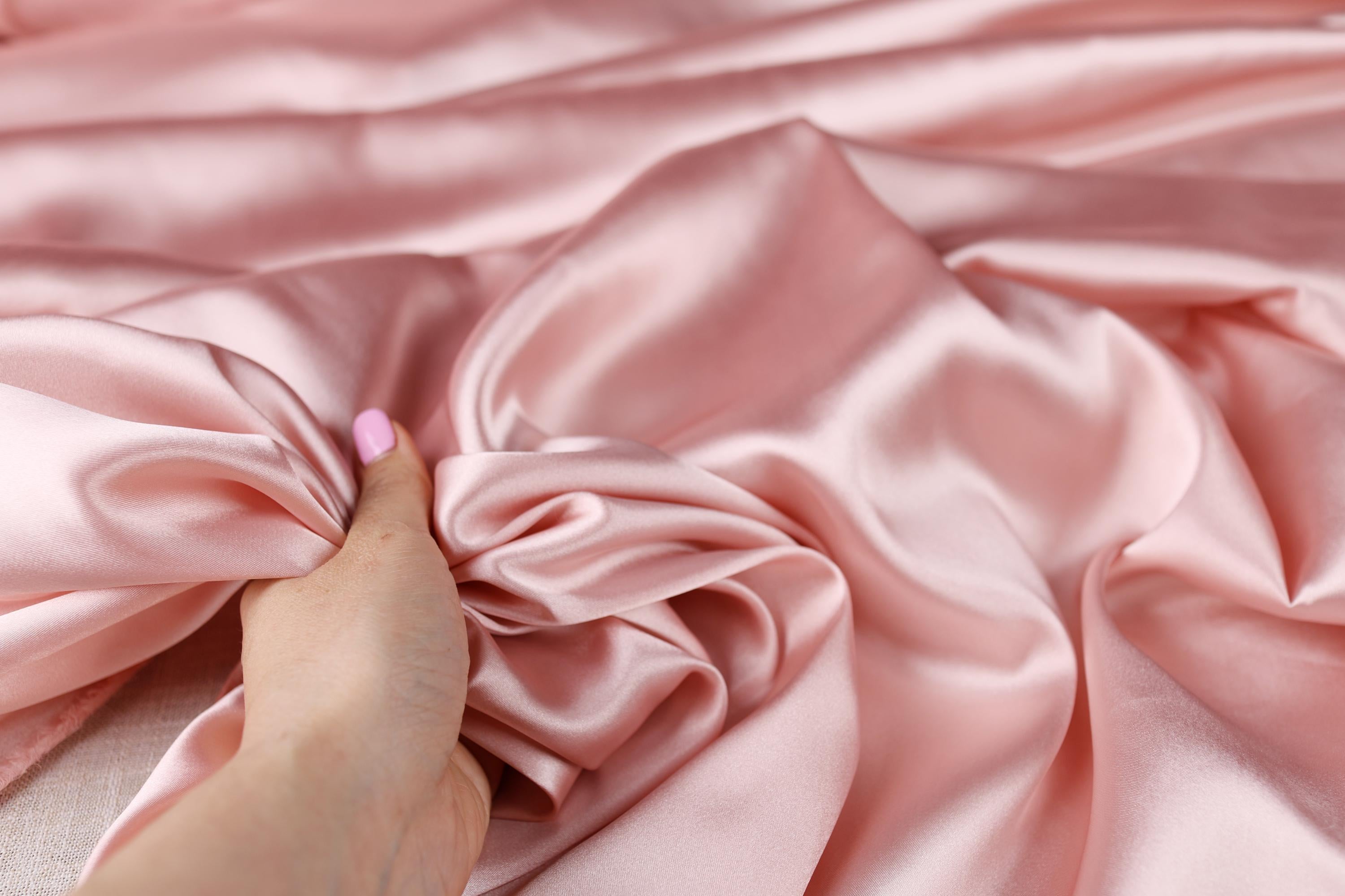 a woman&#39;s hand on a pink satin fabric